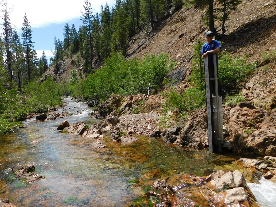 A river in a narrow canyon. A woman works at the top of a high gauge pole.