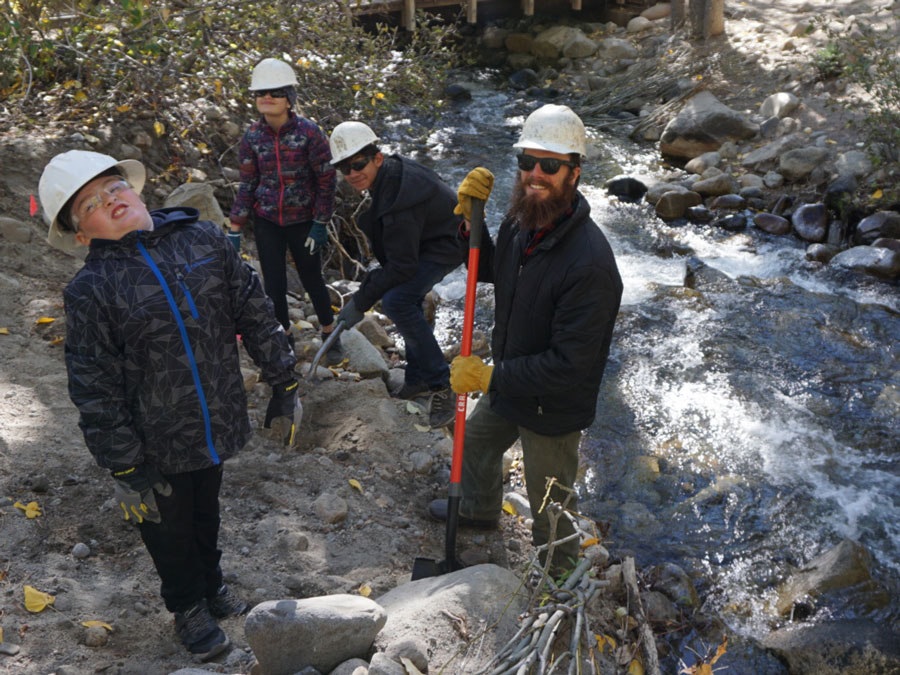 Several children and a man, all wearing safety helmets, by a creek.