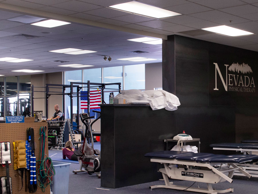 A large room with massage tables on one side of a partial wall and weight equipment on the other side.