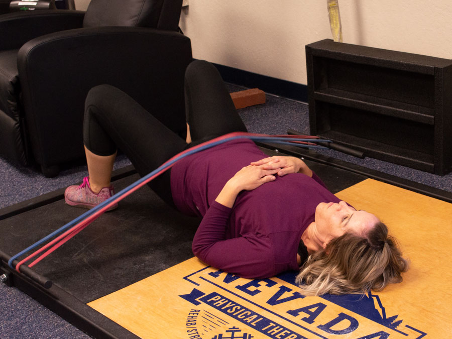 Blonde woman in purple shirt lying on a yellow pad with two rubber bands across her hips.