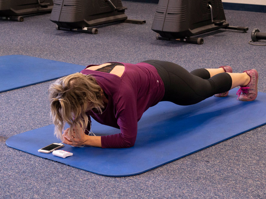 Blonde woman in purple shirt lies above a blue mat, holding herself up by leaning on her elbows.