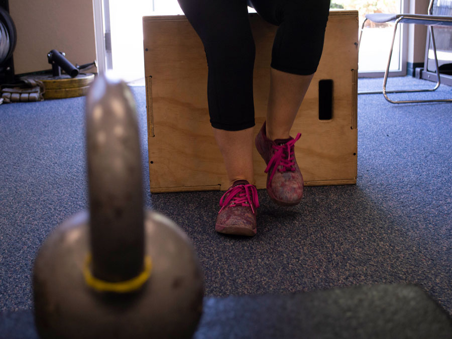 A woman's legs, covered in exercise pants, from the knees down, with purple tennis shoes.