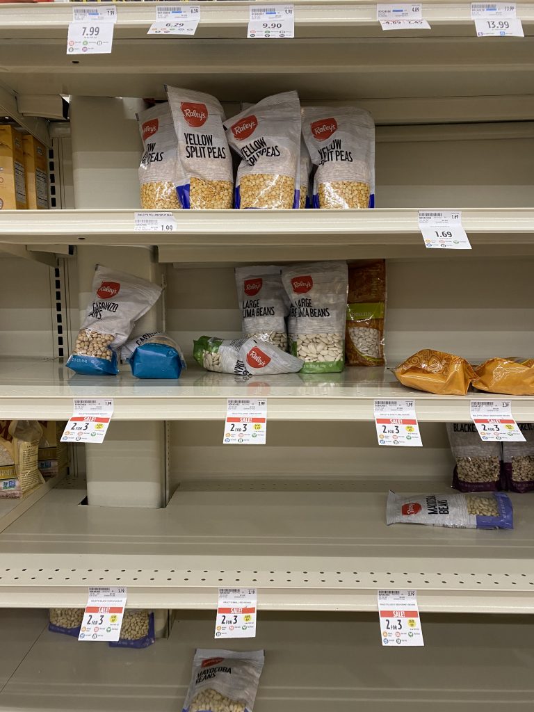 Several nearly empty grocery shelves in the dried bean aisle. Only a few lima beans and garbanzo beans are left. 