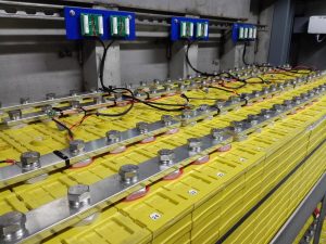 Dozens of large, yellow lithium-ion batteries are bolted together. They are being charged by solar power.