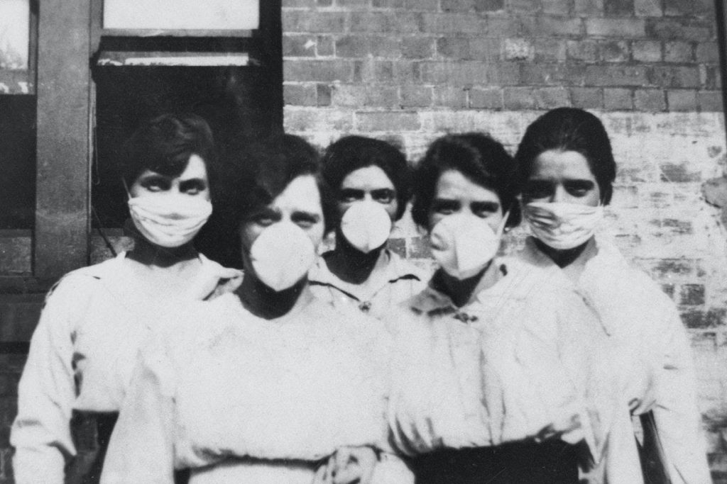 Five women look at the camera while wearing surgical masks over their mouths and noses