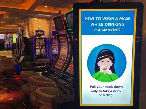 The inside of a glittery casino row of gambling machines and a sign instructing patrons to wear a mask.