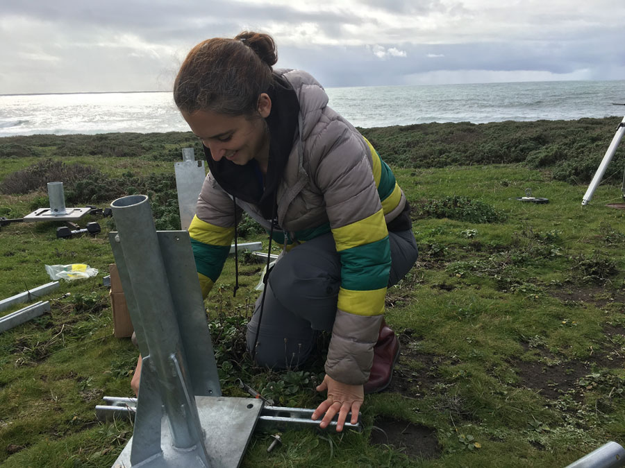 A researcher crouches outside with a large metal piece of equipment