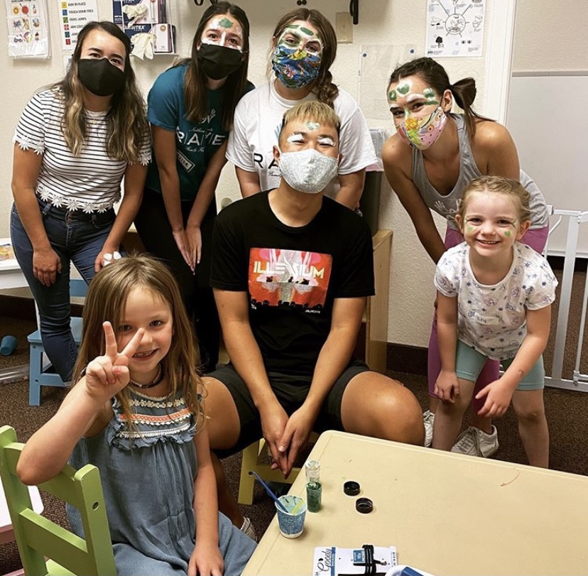 Five people are wearing masks near two children. They all have face paint on their faces.