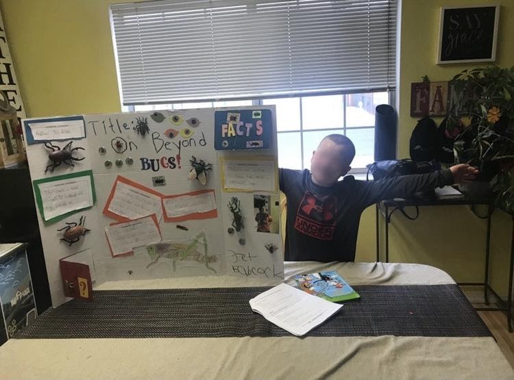 A child stands with his poster board titled "Title: On Beyond Bugs!"