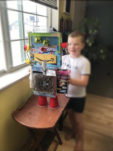 A child stands behind a large robot-like looking structure built out of various things