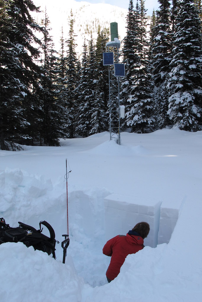 A person sits in a snow pit dug out to check avalanche conditions