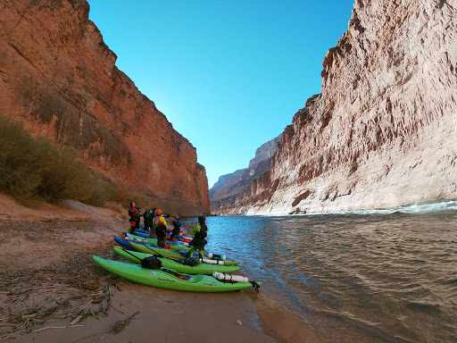Lots of kayaks are sitting on a beach on the bank of a river inside a massive canyon