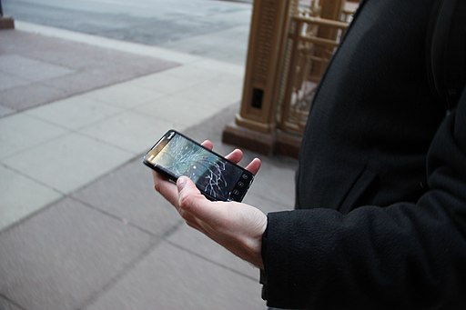 A person holding a smartphone with a broken screen