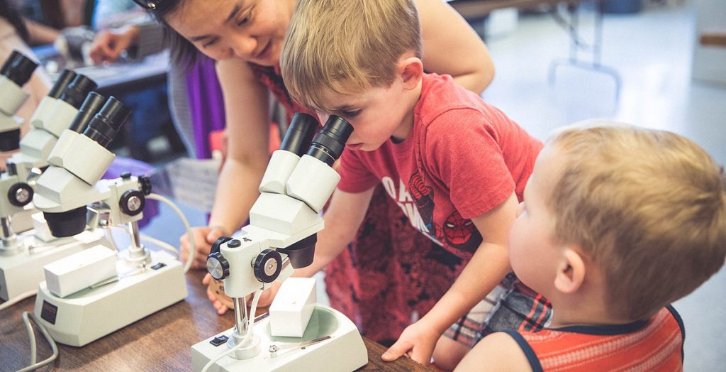 Two children look in a microscope with Jenny Ouyang's help