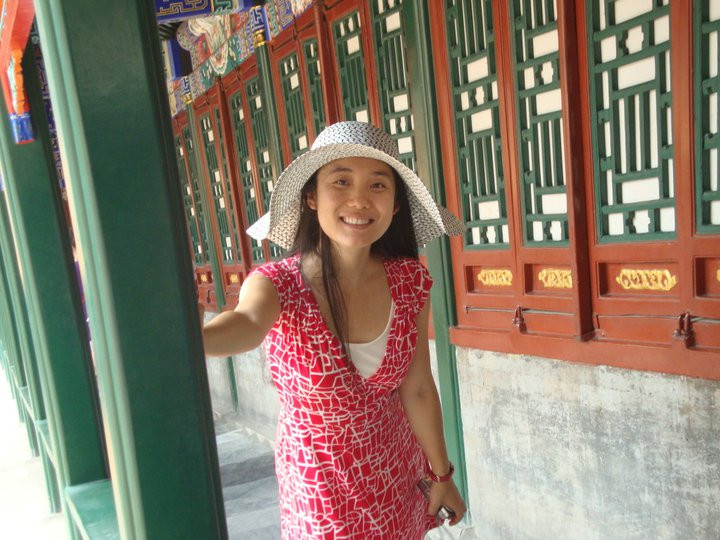 Jenny Ouyang smiles in a red dress and a white hat.