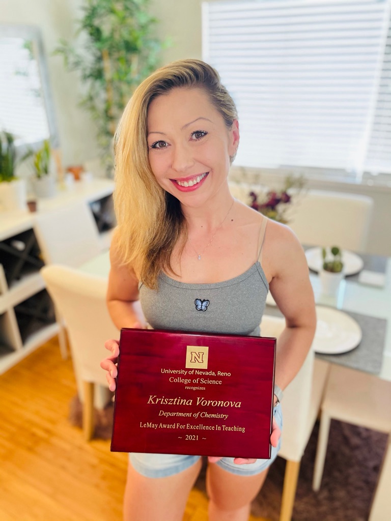 Dr. Krisztina Voronova stands holding her award which reads "University of Nevada, Reno College of Science recognizes Krisztina Voronova, Department of Chemistry, LeMay Award For Excellence In Teaching, 2021"