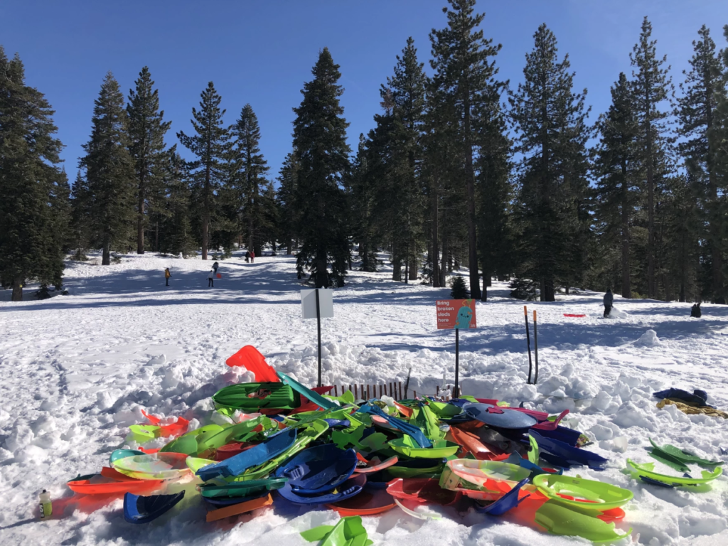 pile of broken plastic sleds in a snowy forested landscape