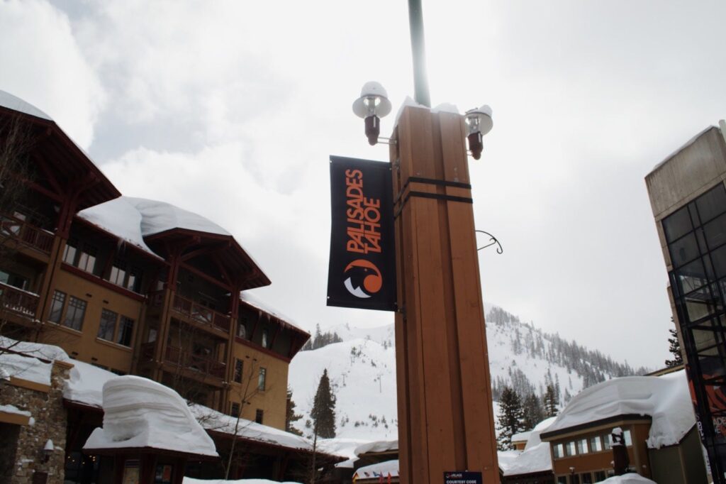 The entrance sign of Palisades Tahoe with snowy buildings in the background