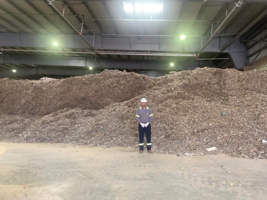 Ivan Valera stands in front of a large mound of shredded landfill waste