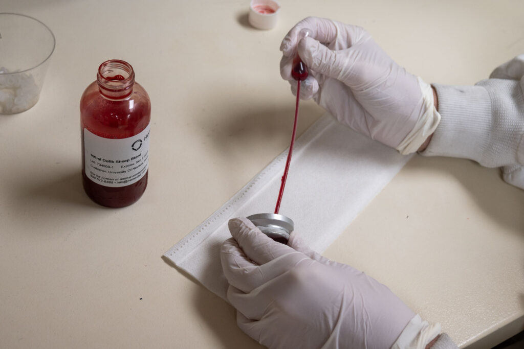 student adds blood from jar to a mosquito feeding device.