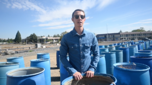 UNR student Otis Clyne stands near blue barrels at agricultural research station