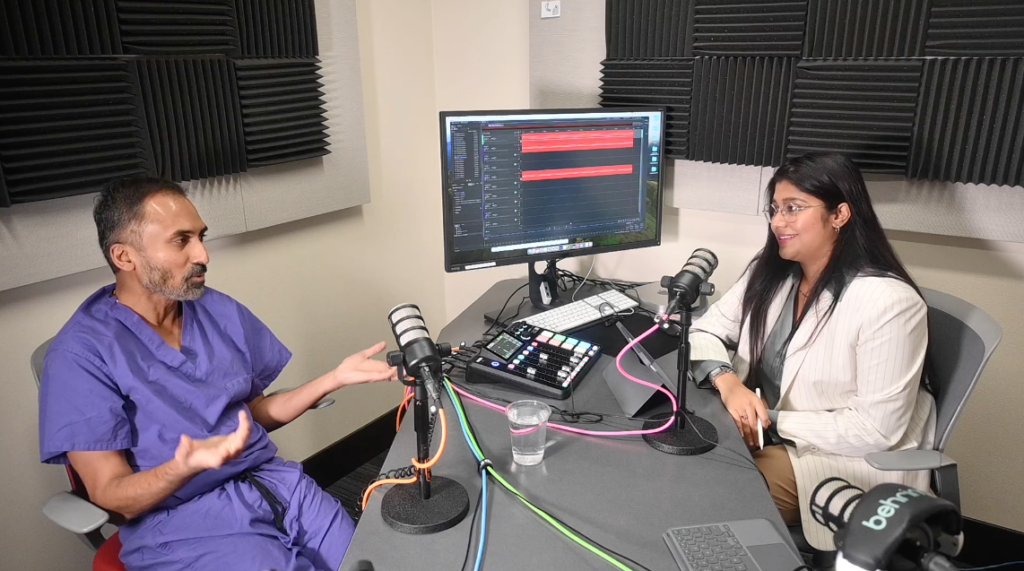 Doctor in purple scrubs is interviewed in recording studio by journalist in white blazer