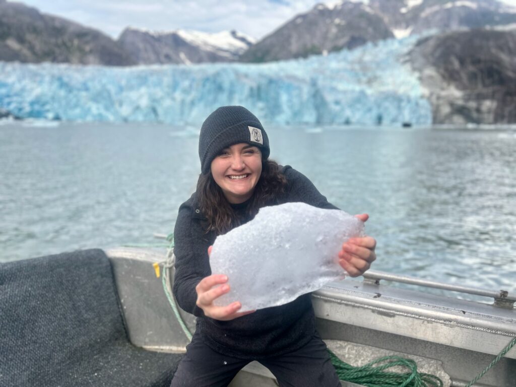 Shelby holding up a piece of ice in front of the LeConte Glacier in Southeast Alaska