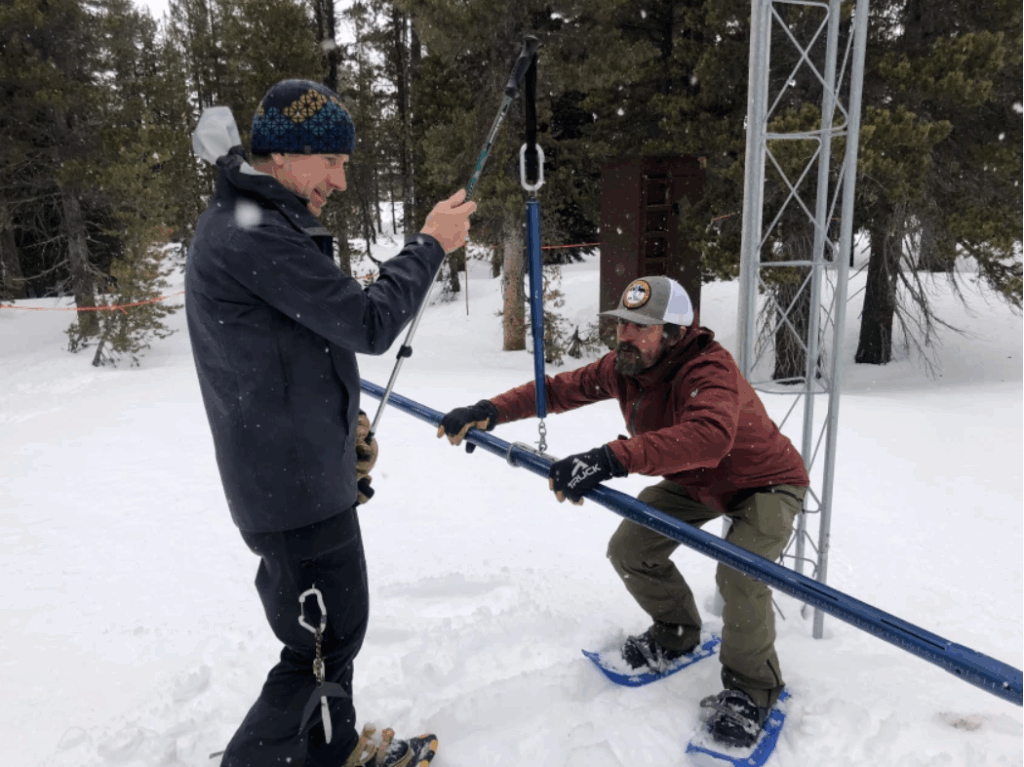 two men measure snowpack in snowy forest