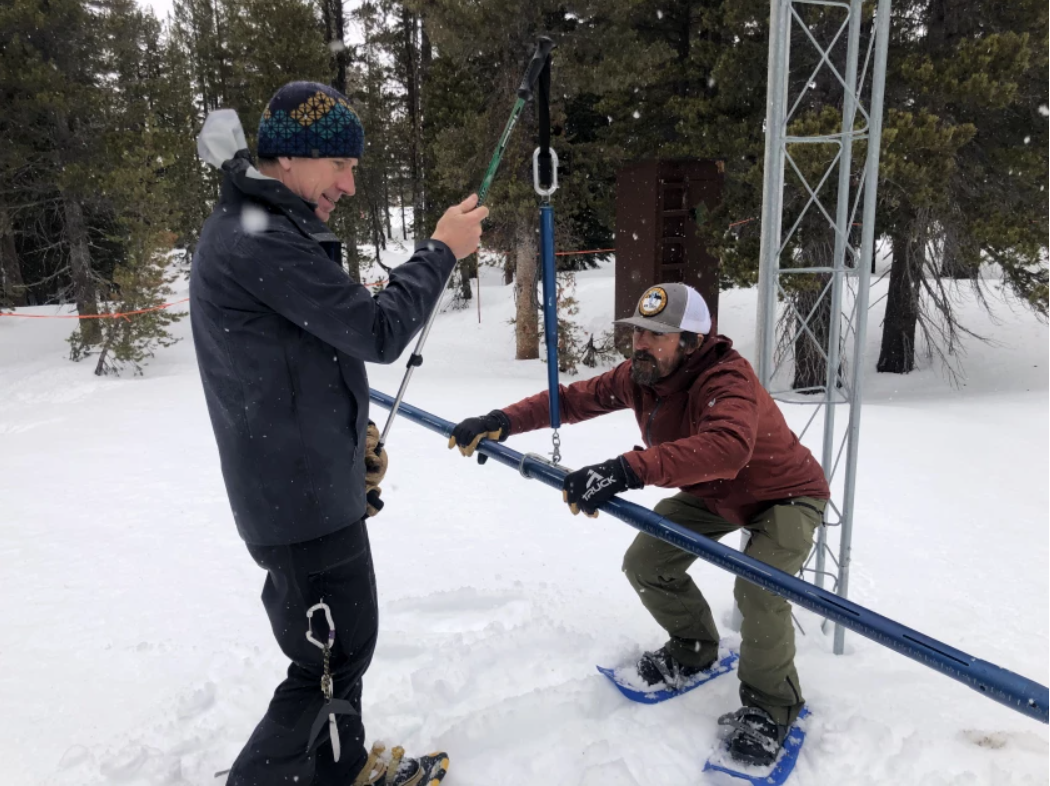 two men measure snowpack in snowy forest