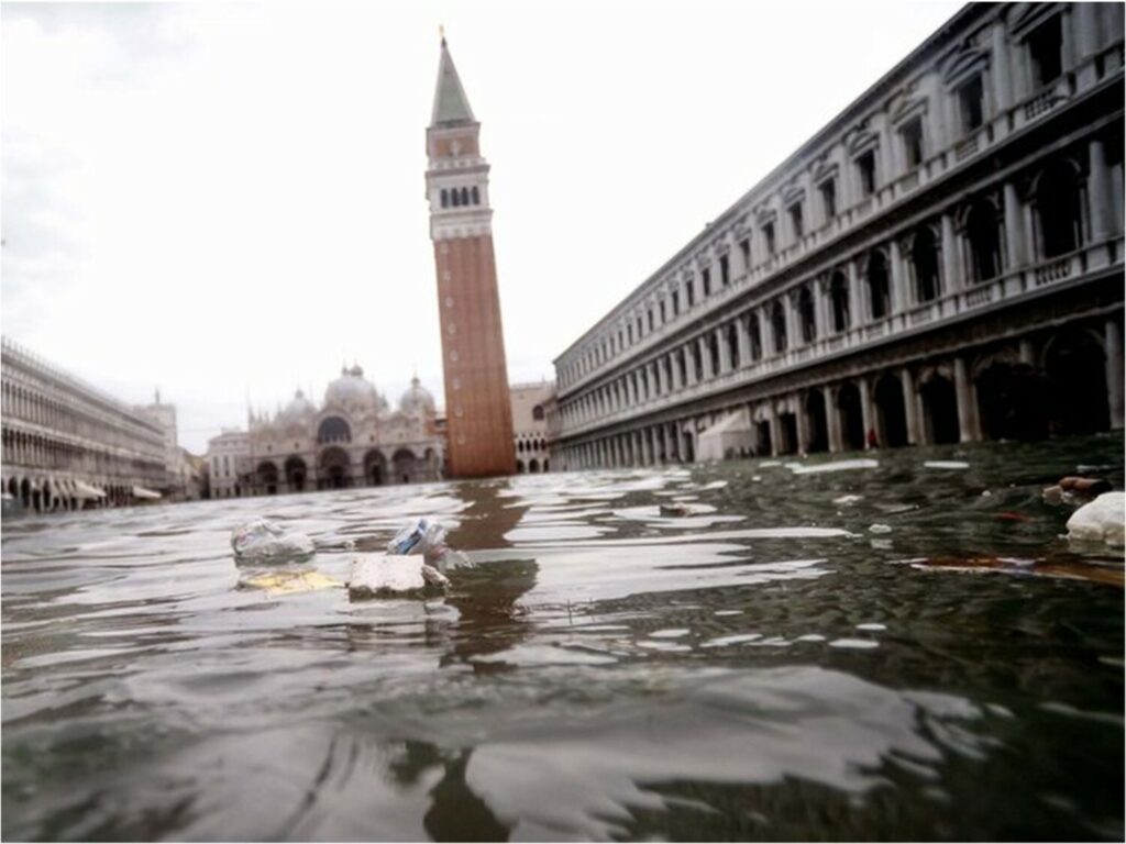 Debris floats in a flooded street in Venice with buildings in the background
