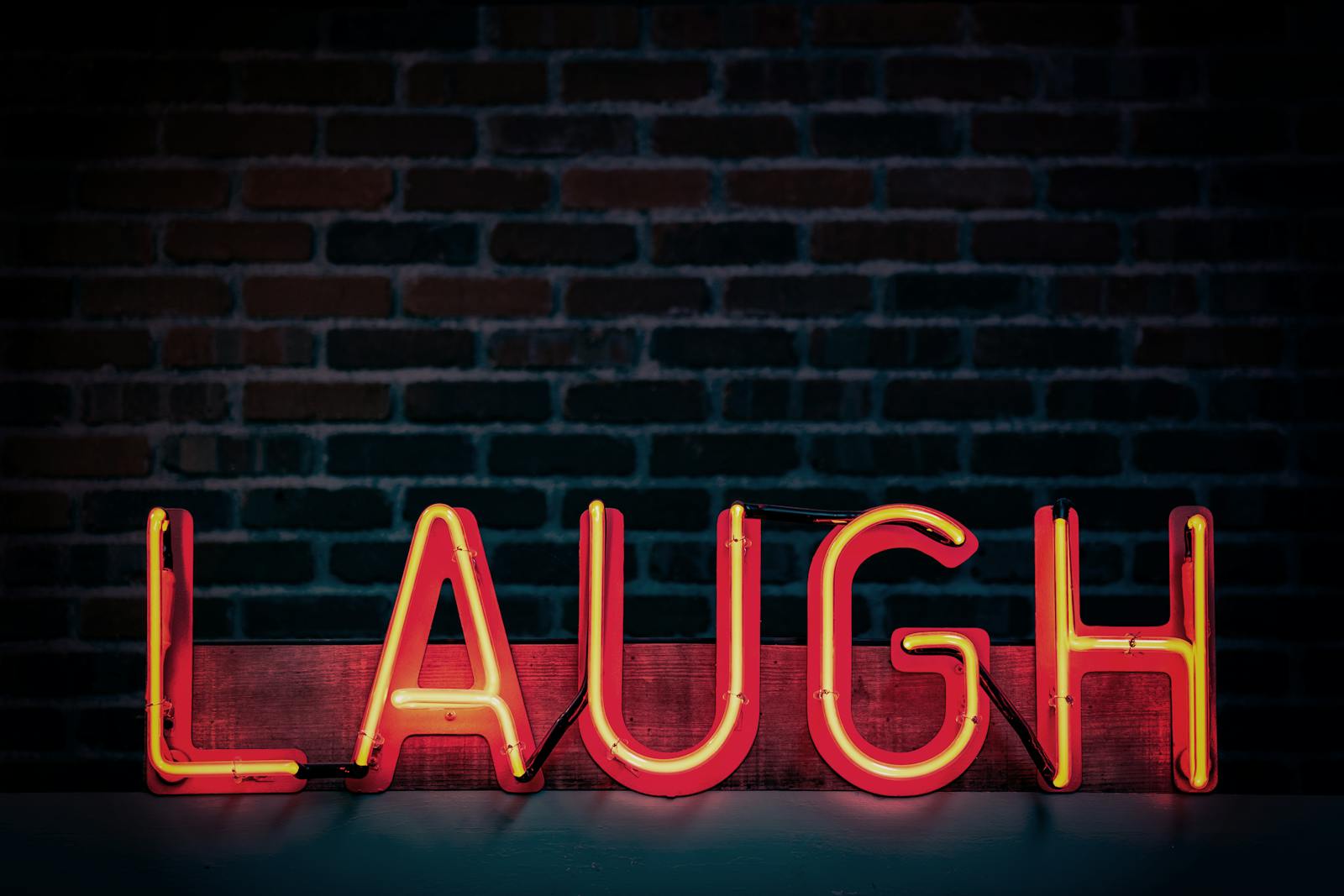 The word "Laugh" is shown in bright red lighting against a dark brick wall