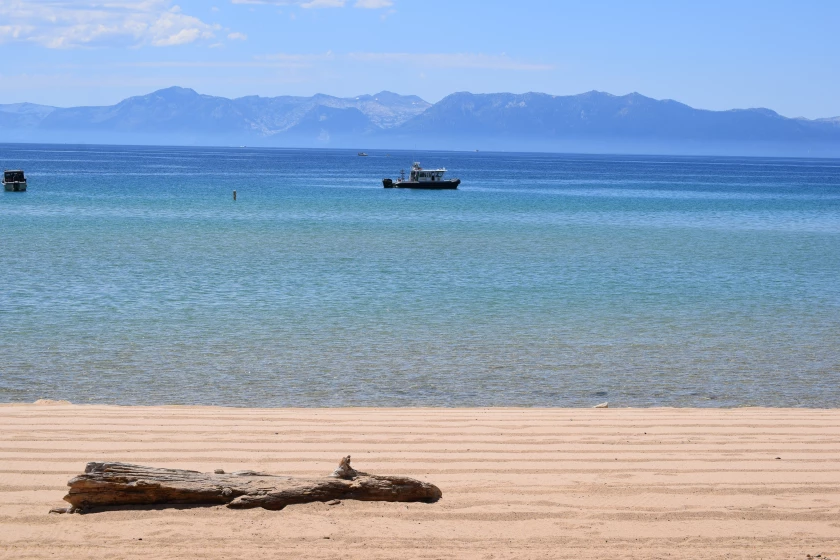 A log sits on the shore of Lake Tahoe with a boat and the mountains sin the distance.