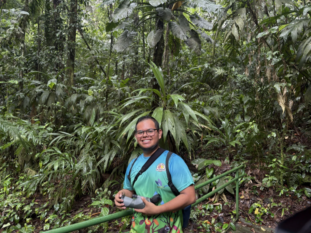 Jeremi Telecaluna stands in rainforest holding spotting scope